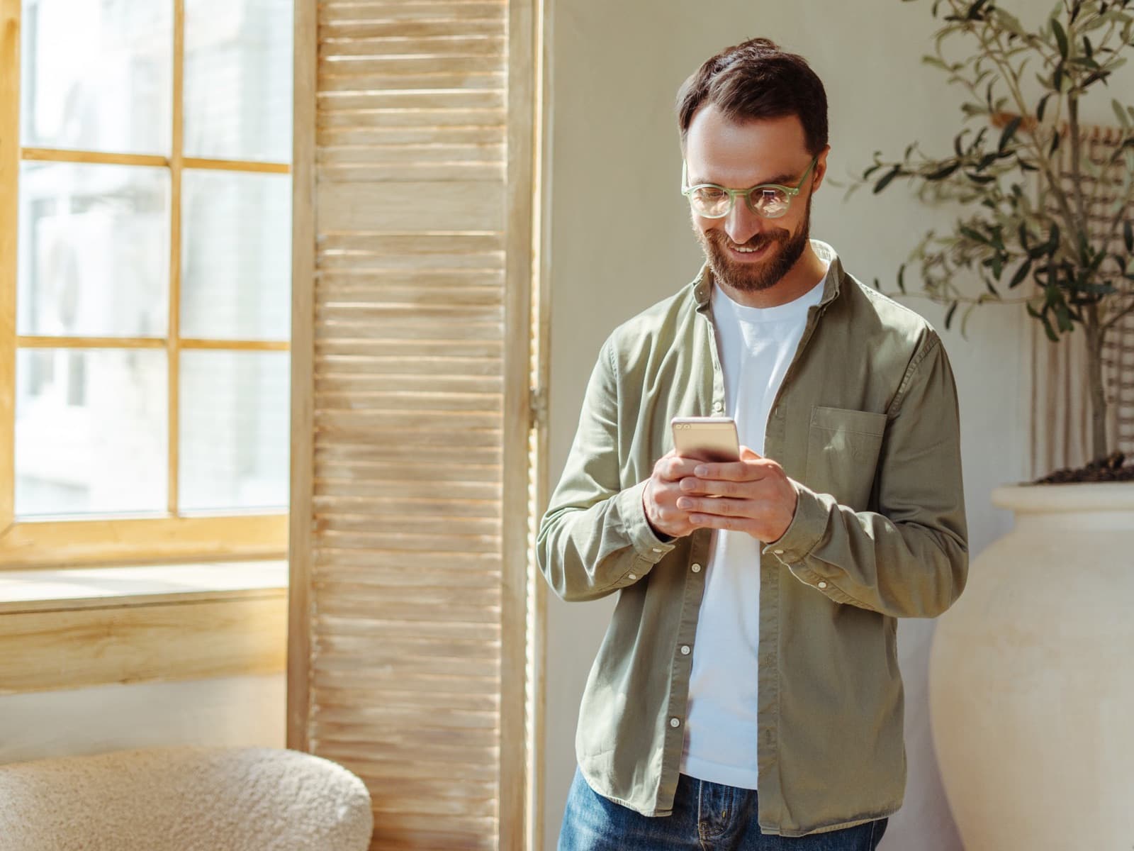 Man smiling at phone in sunny room.